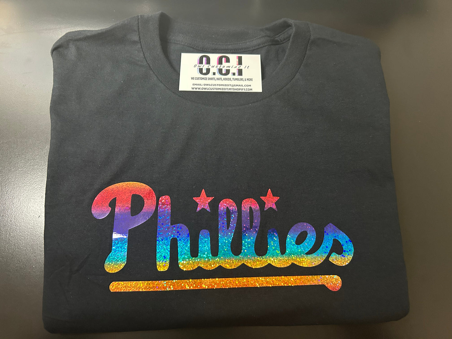 Folded black t-shirt with colorful 'Phillies' text on a metallic surface